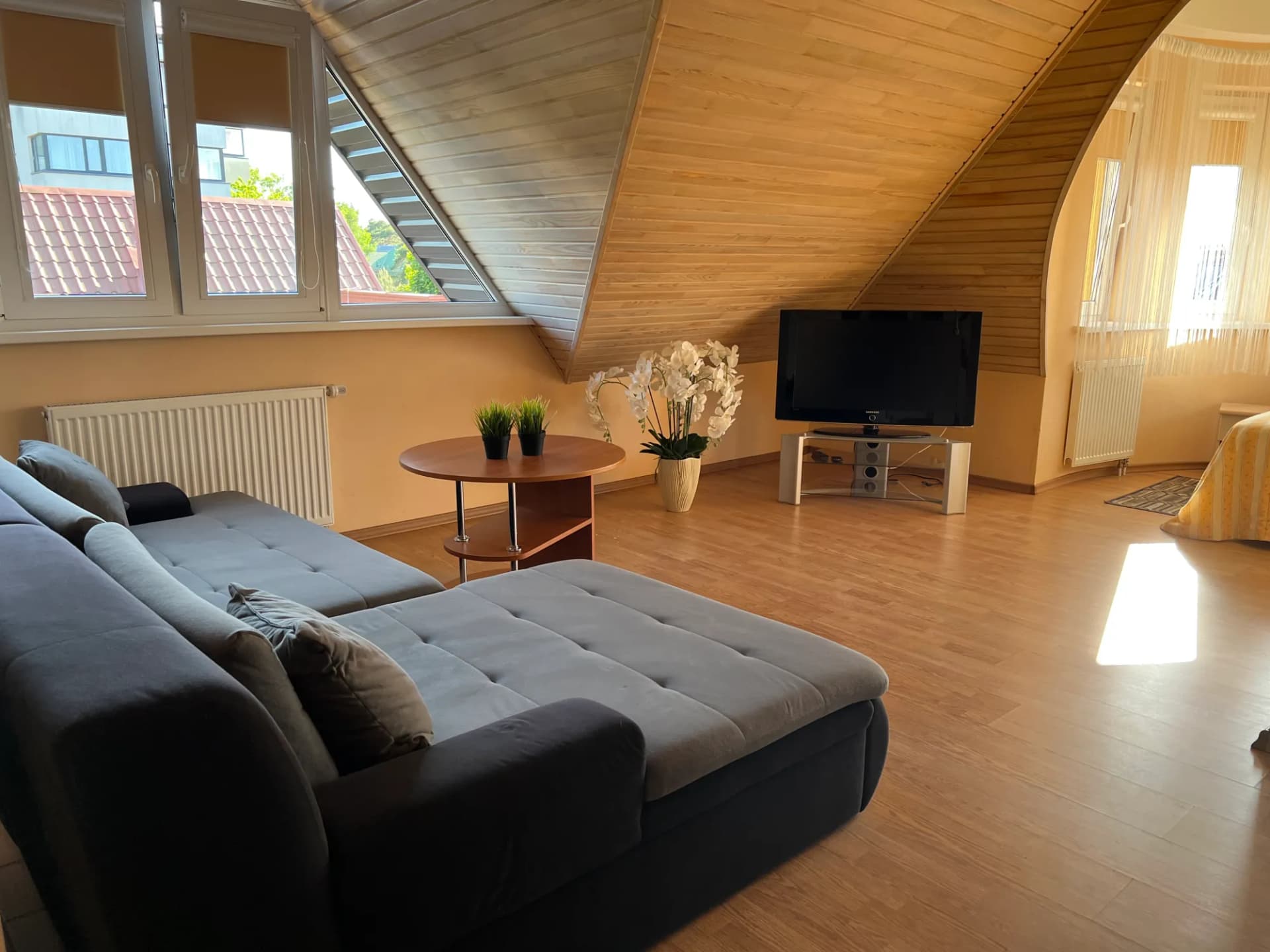 Ketvirtojo kambario mansardinė svetainė su pilka kampine sofa, staliuku ir televizoriumi
